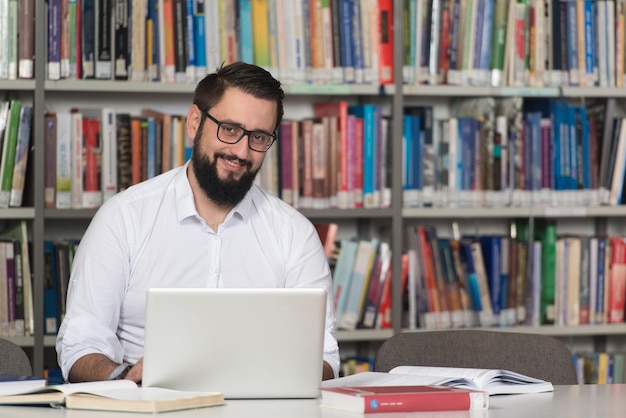 Heureux étudiant masculin avec ordinateur portable dans la bibliothèque