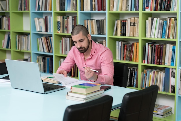 Heureux étudiant masculin avec ordinateur portable dans la bibliothèque