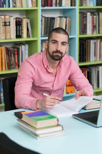 Heureux étudiant masculin avec ordinateur portable dans la bibliothèque