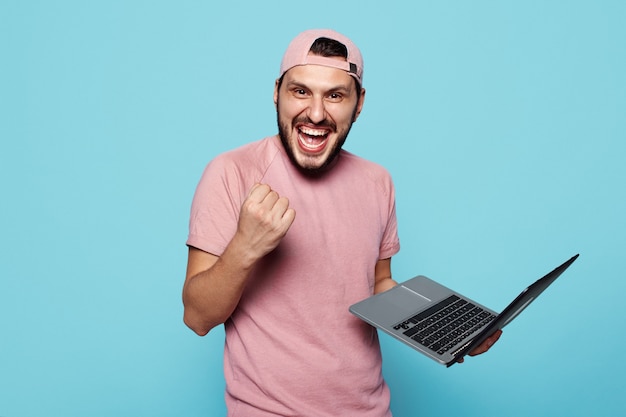 Heureux étudiant tenant le poing de l'ordinateur portable avec succès sur bleu