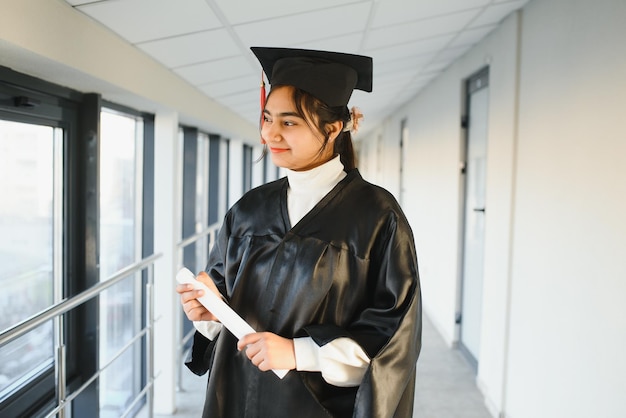 Heureux étudiant universitaire indien en robe de graduation et casquette détenant un certificat de diplôme.