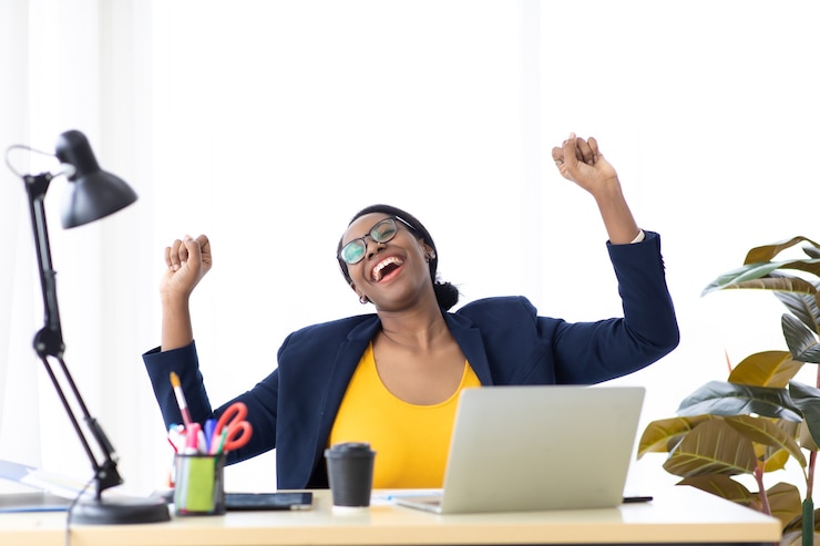 Photo heureux excité réussi belle femme d'affaires afro-américaine triomphant dans un bureau moderne avec ordinateur portable, pose heureuse de succès. travail à domicile