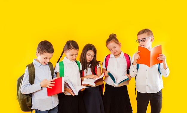 Heureux excités souriants petits élèves tenant des livres de couleur isolés sur fond jaune Retour à l'école