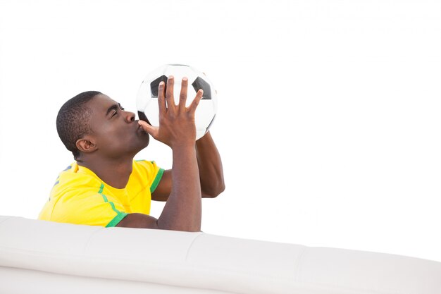 Heureux fan de football brésilien assis sur le canapé baiser la balle