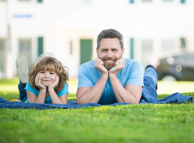 Heureux fils enfant et père homme aime se détendre sur une couverture posée sur l'herbe l'été à l'extérieur, loisirs en famille.