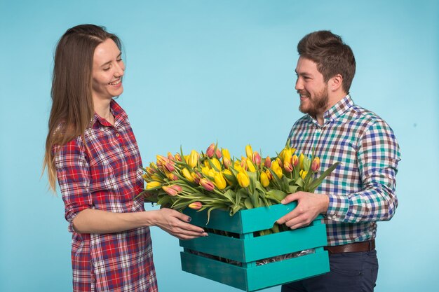 Heureux fleuristes fixant des tulipes dans une grande boîte en bois sur bleu