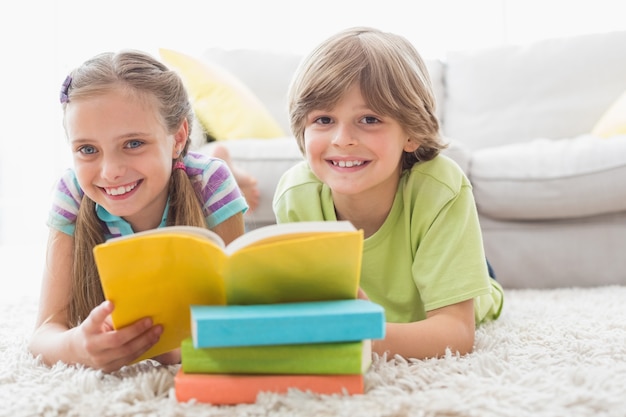 Heureux frères et sœurs réding livre en position couchée sur le tapis