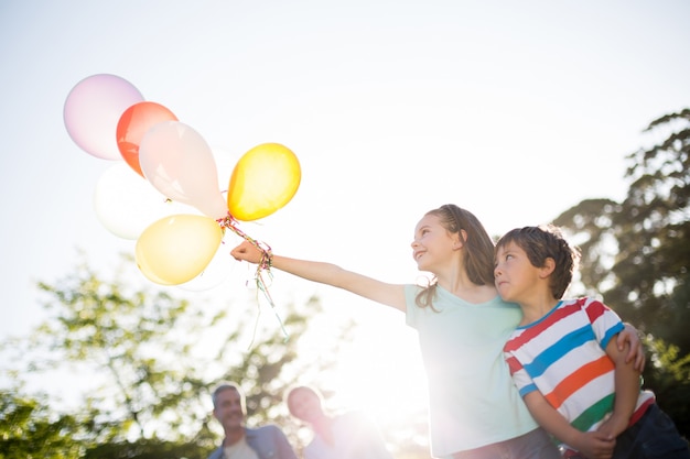 Heureux frères et soeurs tenant des ballons au parc