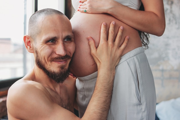 Heureux futur père écoute bébé ventre de sa femme. Couple authentique, famille attend bébé