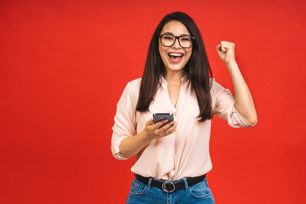 heureux, gagnant, portrait, de, étonné, sourire, occasionnel, femme affaires, tenue, smartphone, isolé, sur, arrière-plan rouge