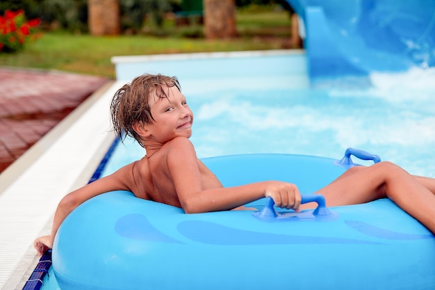 Heureux un garçon de 8 ans monte dans le parc aquatique sur des cercles gonflables sur des toboggans avec éclaboussures