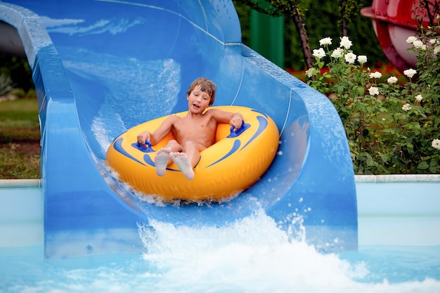 Heureux un garçon de 8 ans monte dans le parc aquatique sur des cercles gonflables sur des toboggans avec éclaboussures