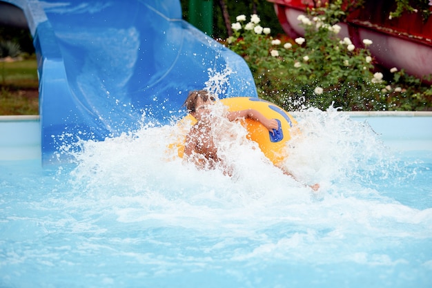 Heureux un garçon de 8 ans monte dans le parc aquatique sur des cercles gonflables sur des toboggans avec éclaboussures