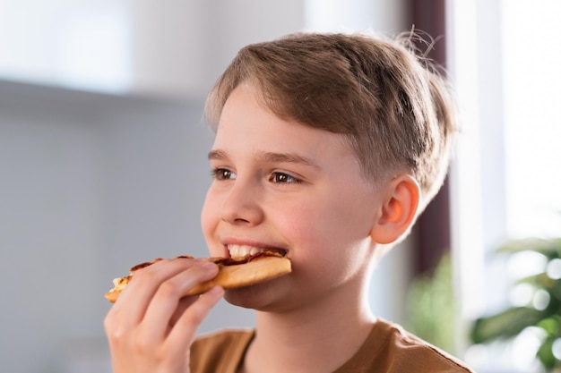 Heureux garçon adolescent appréciant de manger de délicieuses pizzas à la maison Portrait d'un adolescent mignon