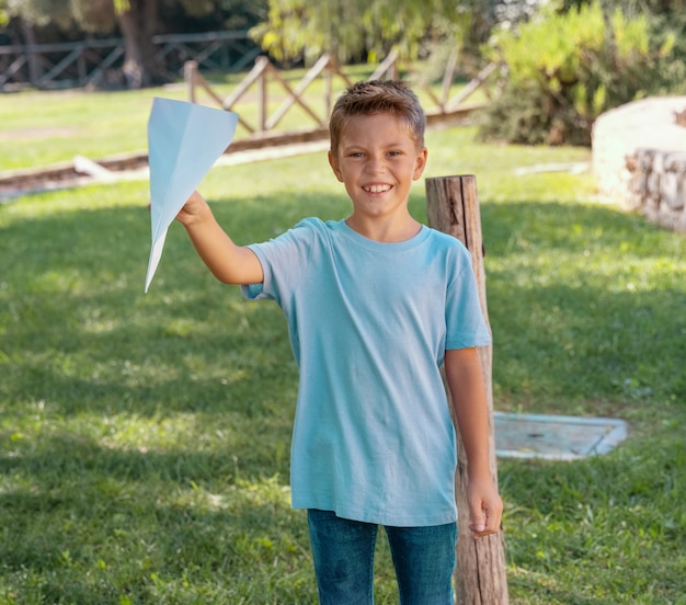 Photo heureux garçon d'âge préscolaire joue avec un avion en papier dans un parc