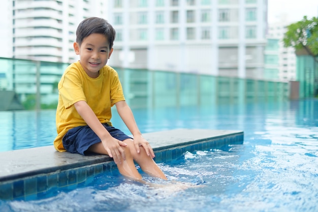 Heureux garçon asiatique assis piscine