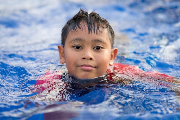 Heureux garçon asiatique nageant sur une piscine en été
