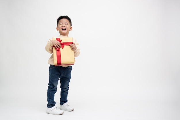 Heureux garçon asiatique souriant et tenant une boîte-cadeau en or isolée sur fond blanc. Concept de nouvel an et de Noël