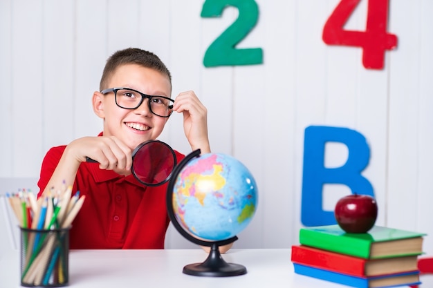 Heureux garçon assis au bureau avec globe, pomme et livres