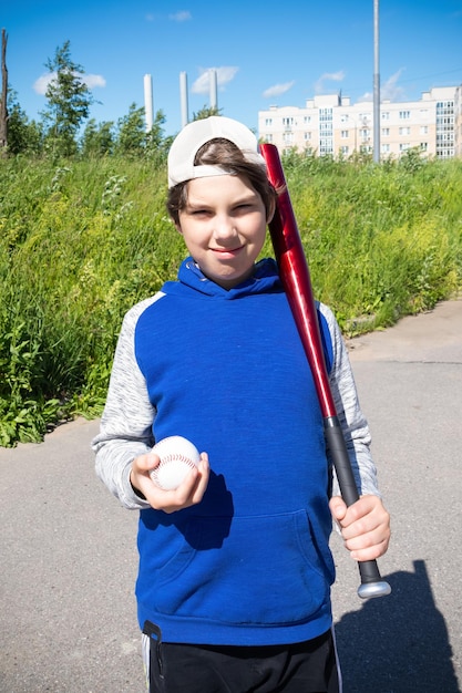 Heureux garçon avec batte de baseball et balle contre l'herbe verte à l'extérieur par une journée ensoleillée