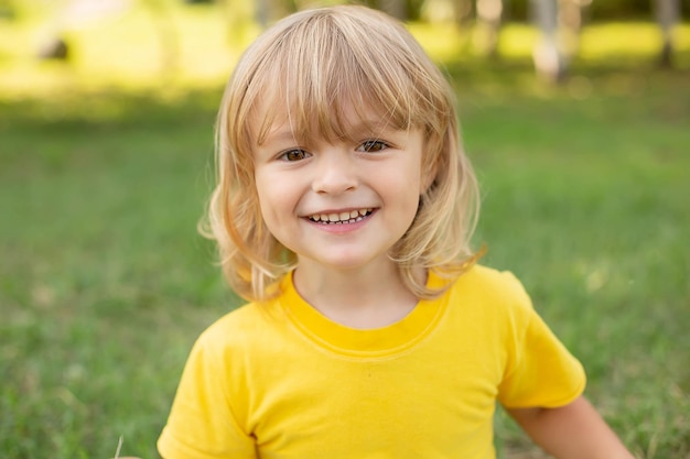 heureux garçon blond assis sur la pelouse dans un T-shirt jaune sourire à pleines dents