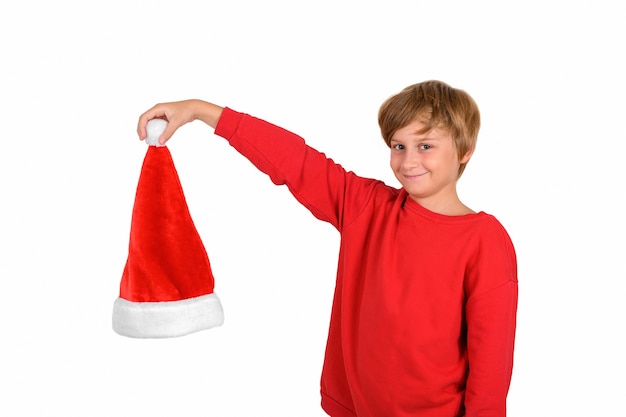 Heureux garçon blond souriant en pull rouge tenant et montrant un bonnet de noel