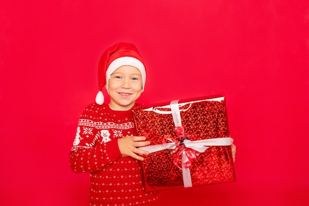 Heureux garçon dans un chandail et bonnet de Noel tenant un cadeau