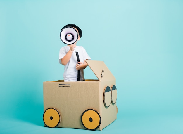 Heureux garçon d'enfants asiatiques en conduisant jouer à l'imagination de la boîte en carton avec un mégaphone