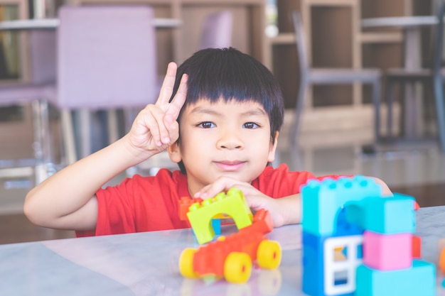 Heureux garçon entouré de blocs de jouets colorés vue de dessus en forme de V main pour la victoire