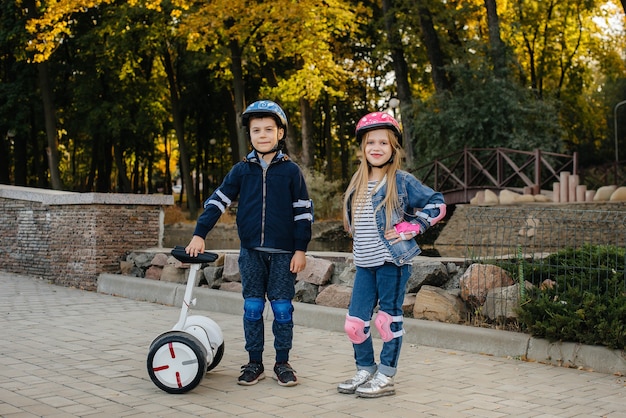 Heureux garçon et fille debout et monter dans le parc en Segway et scooters pendant le coucher du soleil