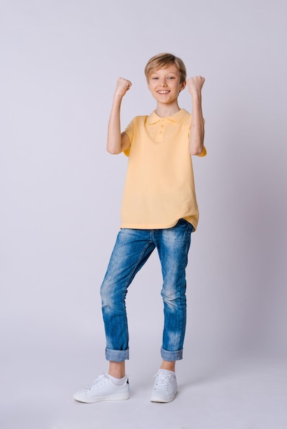 Heureux garçon Mains levées les mains dans le bonheur portant un t-shirt jaune et un jean