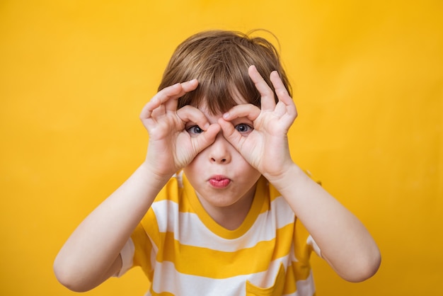 Heureux garçon mignon enfant regardant la caméra à travers les doigts sur fond jaune