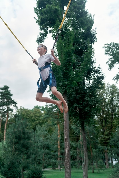 Heureux garçon riant suspendu à des élingues saute haut sur un trampoline dans un parc d'attractions