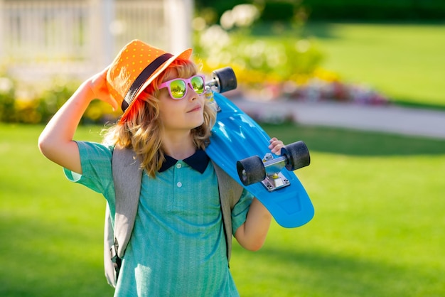 Heureux garçon riant et tenant le portrait d'enfants de mode d'été en plein air de planche à roulettes