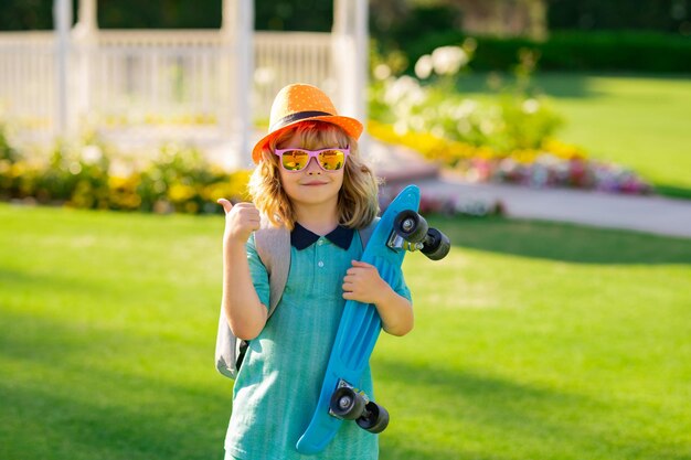 Heureux garçon riant et tenant le portrait d'enfants de mode d'été en plein air de planche à roulettes