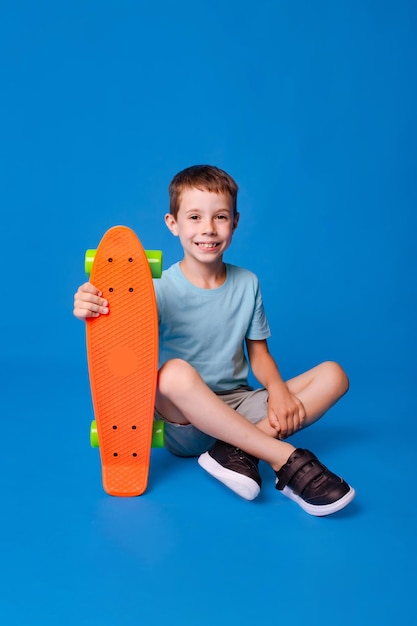 heureux garçon souriant dans une maquette bleue T-shirt tenant un skateboard isolé sur fond bleu clair de studio