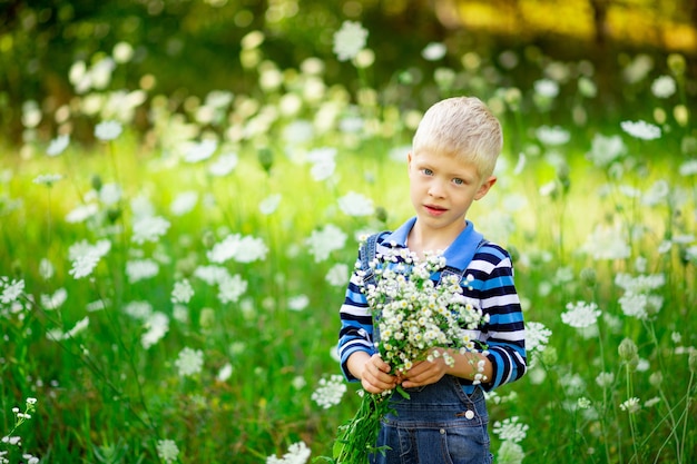 Heureux garçon sur le terrain avec des fleurs tenant un bouquet de fleurs