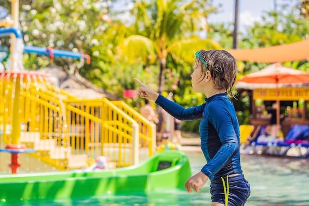 Heureux garçon sur toboggan aquatique dans une piscine s'amusant pendant les vacances d'été dans une belle