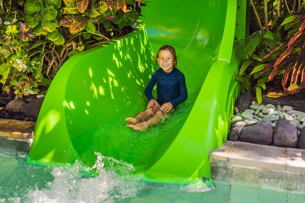 Photo heureux garçon sur toboggan aquatique dans une piscine s'amusant pendant les vacances d'été dans un magnifique complexe tropical