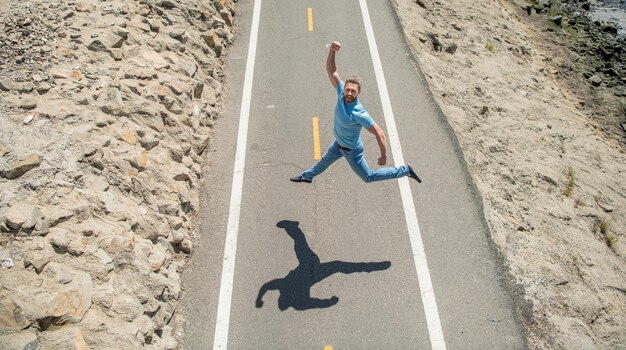 Heureux gars athlétique mature sautant sur la route en plein air, émotions