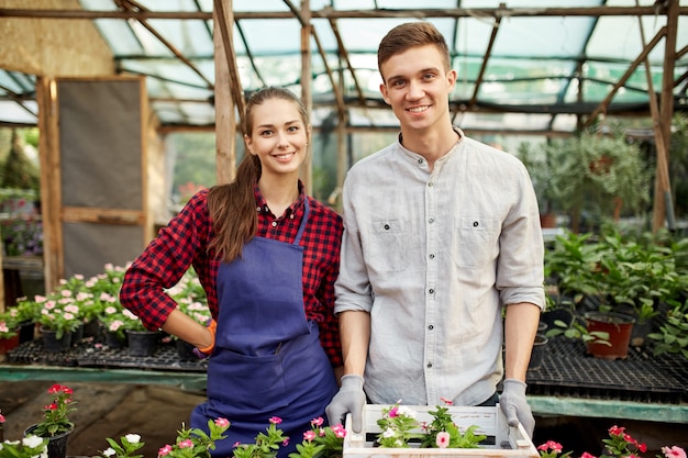 Heureux gars et fille jardiniers sable à côté des pots avec des semis de fleurs en serre par une journée ensoleillée. .