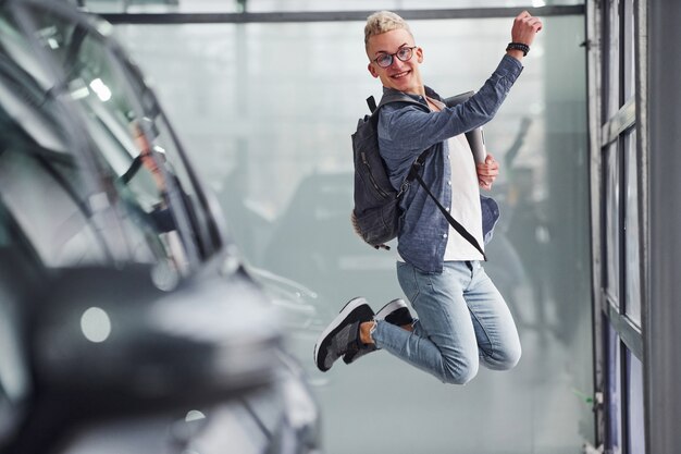 Heureux gars hipster sautant à l'intérieur et près de la voiture