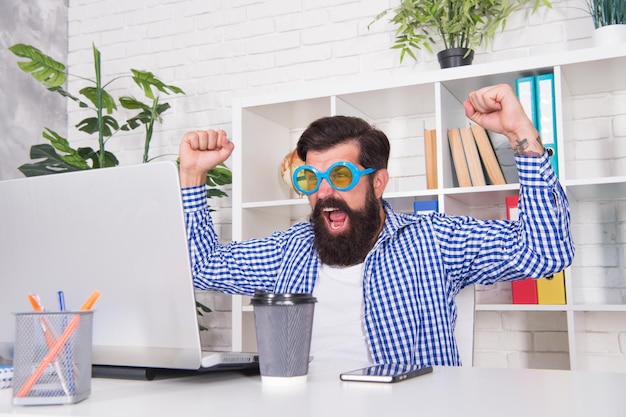 Heureux gestionnaire hurlant faisant le geste du gagnant regardant l'écran de l'ordinateur portable dans un bureau moderne, gagnant.