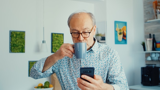 Heureux grand-père écoutant de la musique et dansant tout en prenant son petit-déjeuner dans la cuisine avec des lunettes Danse senior détendue, mode de vie amusant avec la technologie moderne