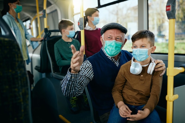 Heureux grand-père et petit-fils parlant tout en portant des masques faciaux et en faisant la navette en bus ensemble