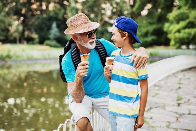 Heureux grand-père s'amusant avec son petit-fils tout en mangeant des glaces à l'extérieur dans le parc.