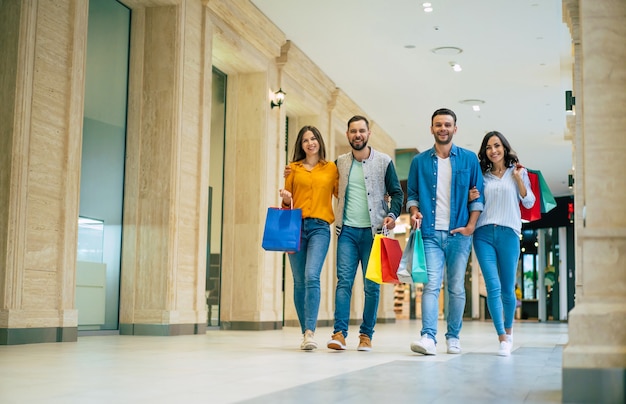 Heureux groupe d'amis beaux et élégants modernes excités dans des vêtements décontractés avec des sacs en papier se promènent dans le centre commercial pendant les achats.