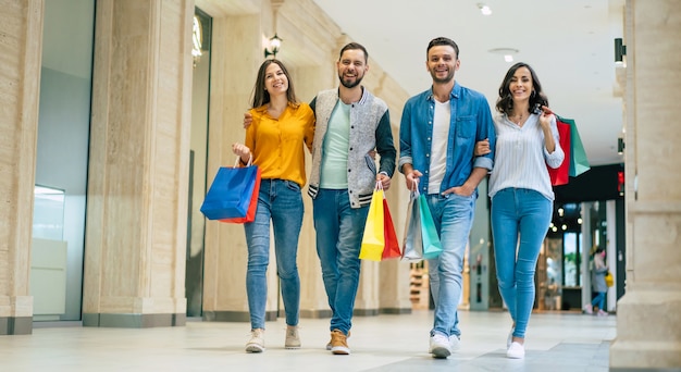 Heureux groupe d'amis beaux et élégants modernes excités dans des vêtements décontractés avec des sacs en papier se promènent dans le centre commercial pendant les achats.