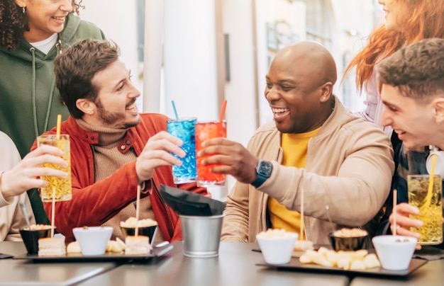 Heureux groupe d'amis multiraciaux toast boire et manger au restaurant réunion Concept de style de vie avec des amis hipster partageant l'happy hour ensemble Mise au point sélective