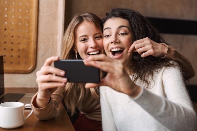 heureux heureux jolies filles amis assis dans un café à l'aide d'un téléphone portable